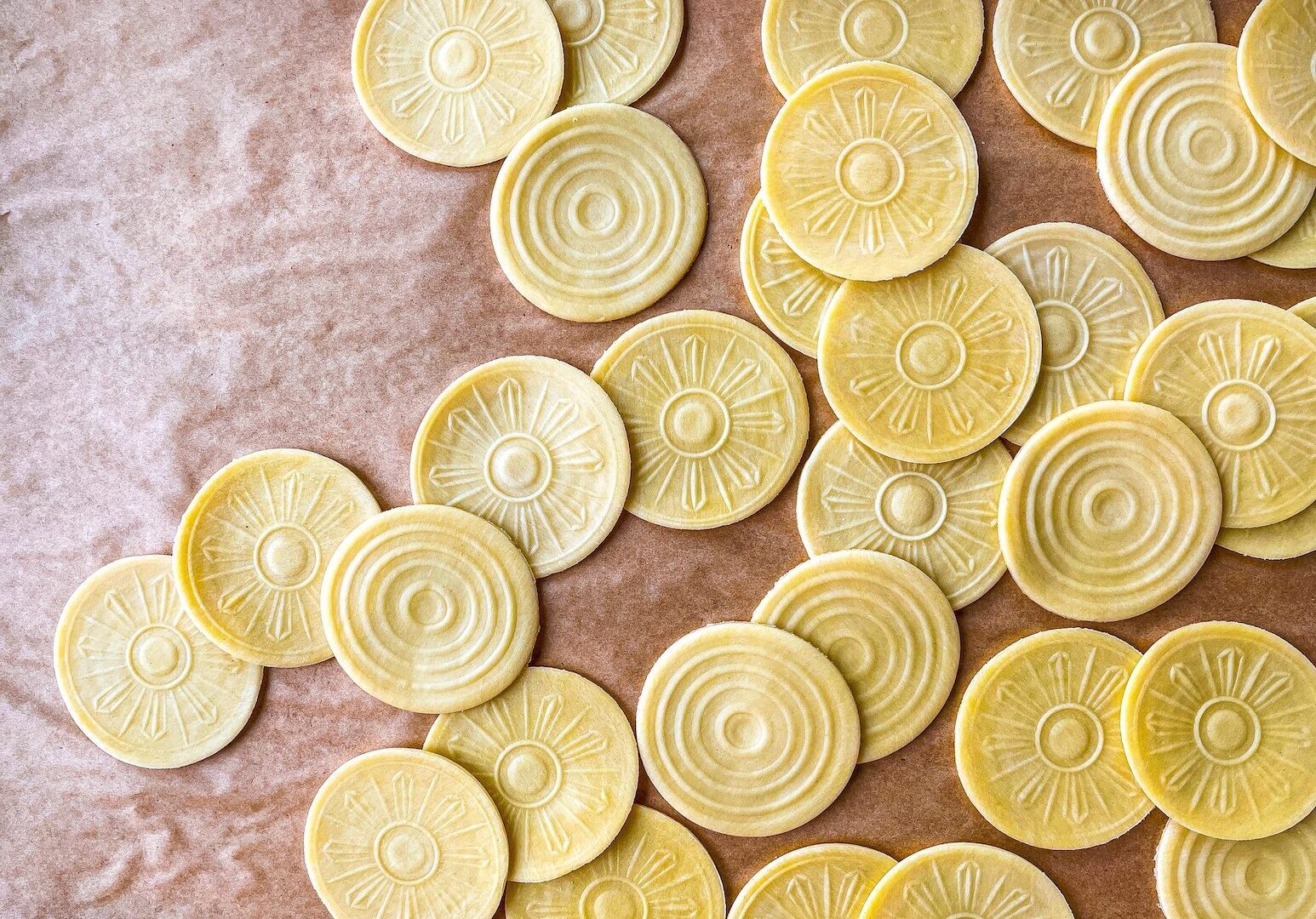 Round pasta medallions are spread out across parchment paper. Each pasta medallion, known as "corzetti", as a patterned design.