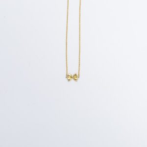 There is a small gold pendant-style necklace, hanging in the top part of the photo. In the center is a small farfalle pasta pendant, suspended on a gold cable chain.