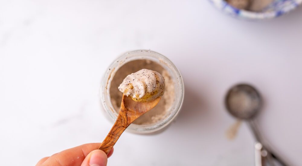 Bird's eye view of a hand holding a small wooden spoon, scooping out a creamy gelato from the top of a mason jar.