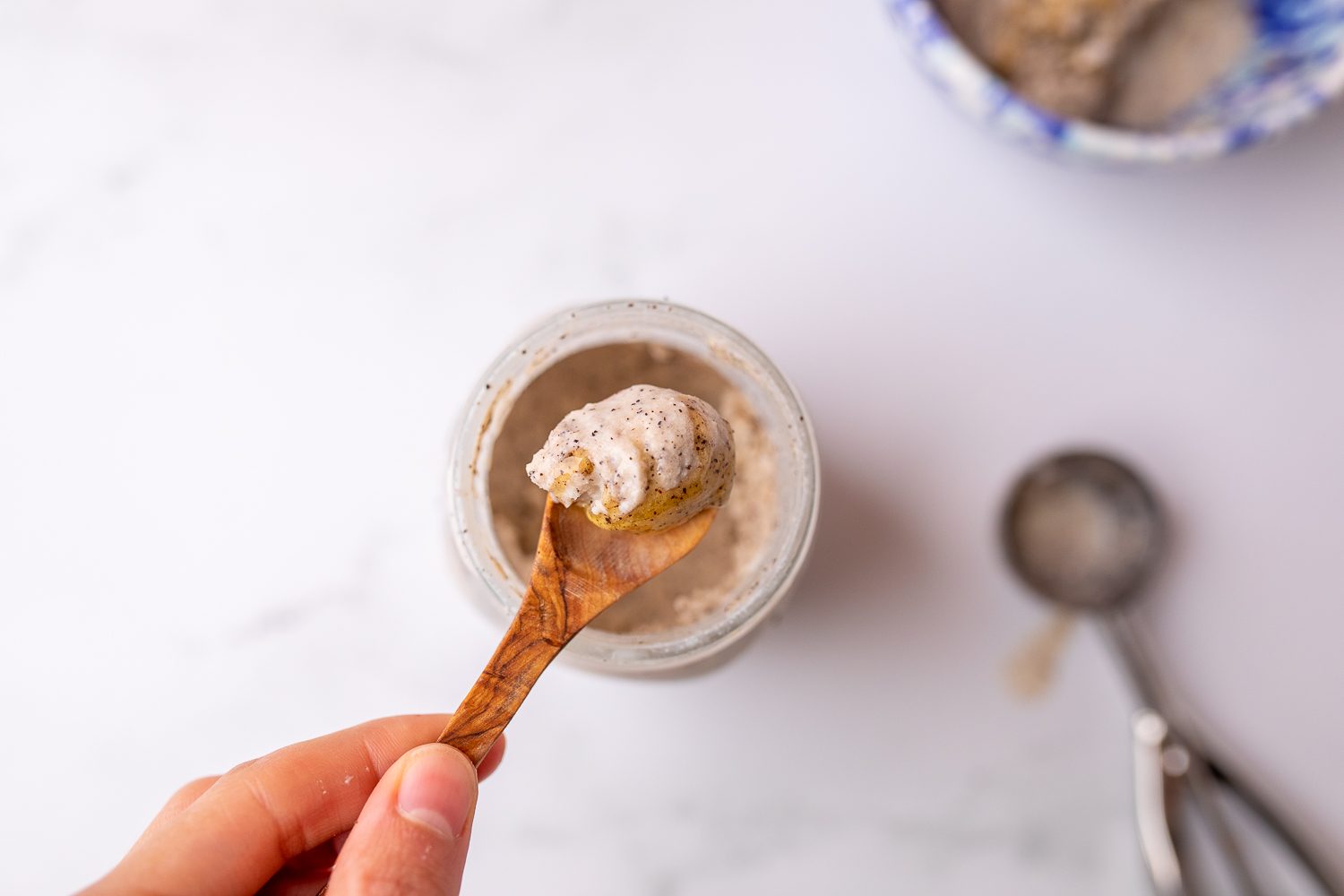 Bird's eye view of a hand holding a small wooden spoon, scooping out a creamy gelato from the top of a mason jar.