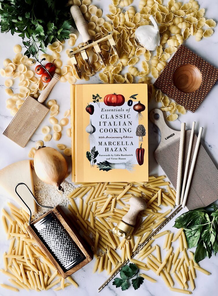 Marcella Hazan book surrounded by pasta, pasta tools and herbs