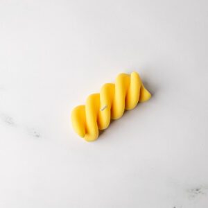 Yellow corkscrew pasta candle on a marble background.